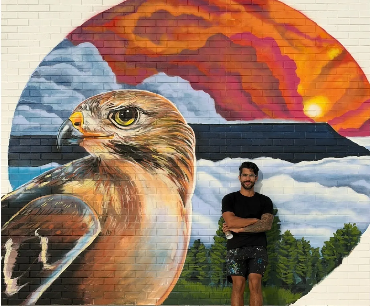 Artist standing in front of a detailed hawk mural